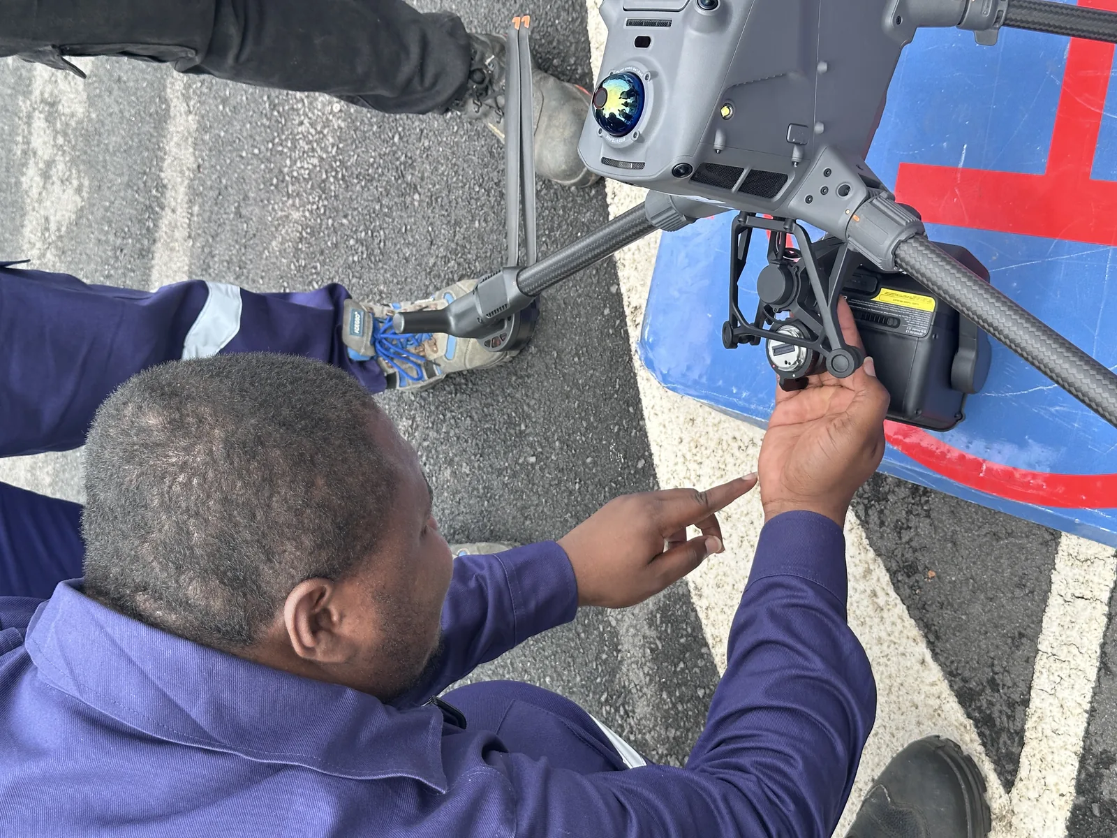 Mains montant un capteur sur le bras d'un drone posé sur sa plateforme