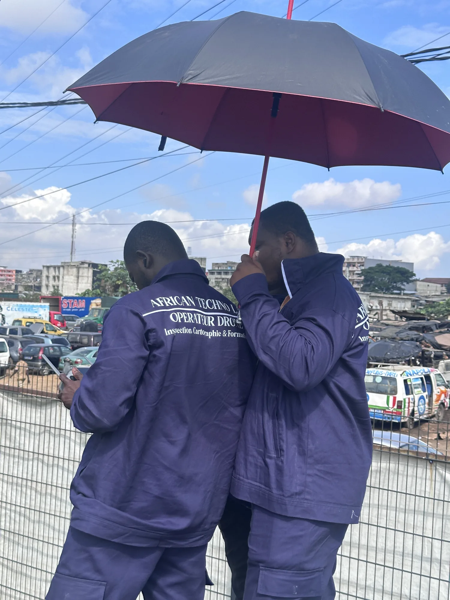 Deux opérateurs en combinaison African Techno Lab pilotant sous un parasol, en ville